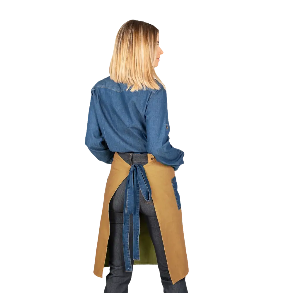 Una donna che indossa una camicia di jeans blu, pantaloni scuri e un grembiule abbronzato con lacci di jeans blu.