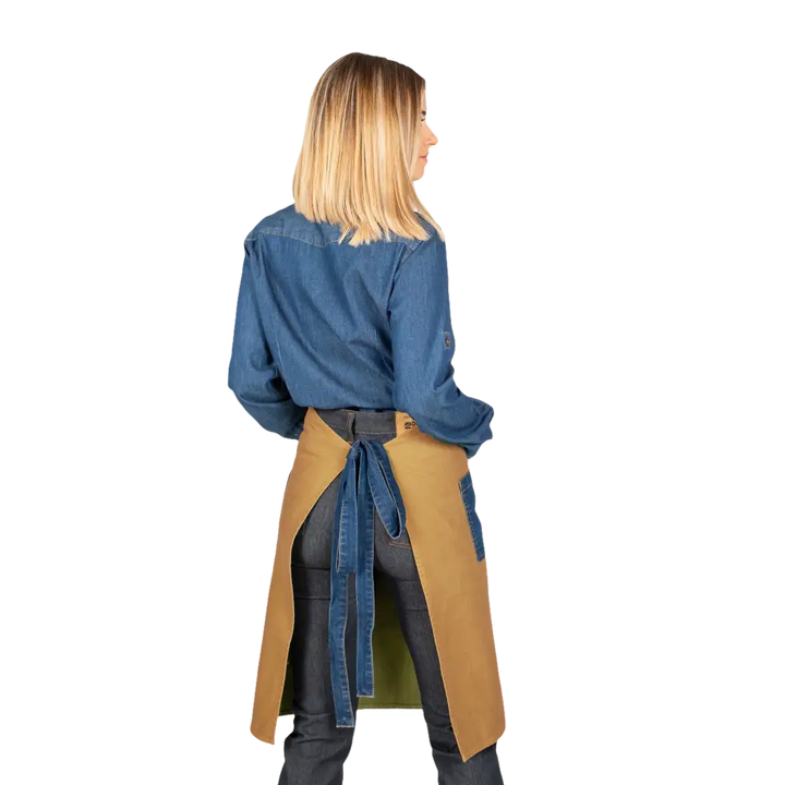 Una donna che indossa una camicia di jeans blu, pantaloni scuri e un grembiule abbronzato con lacci di jeans blu.