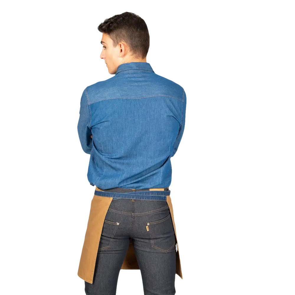 Un giovane con camicia di jeans blu e jeans scuri, che indossa un mezzo grembiule abbronzato.
